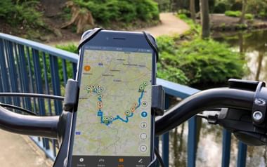 iPhone am Fahrradlenker befestigt zeigt Radweg-Navigationsapp mit blauer Routenlinie und Standortmarkierungen auf der Karte.