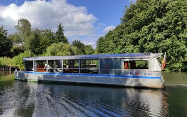 Modernes solarbetriebenes Passagierboot namens Solaris mit blauem Metallrumpf und Solarpaneelen auf dem Dach, auf ruhigem grünen Wasserweg bei Münster.