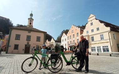 Zwei grüne Fahrräder auf dem gepflasterten Marktplatz in Riedenburg mit bunten historischen Gebäuden und einem Kirchturm im Hintergrund.