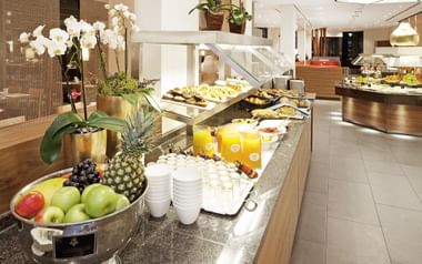 Elegantes Frühstücksbuffet im Hotel Mövenpick Münster mit frischen Früchten, Säften und warmen Speisen. Weiße Orchideen und modernes Design.