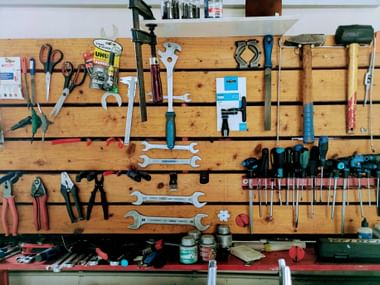 Wooden pegboard wall displaying organized bicycle repair tools including wrenches, screwdrivers, pliers, and various bike maintenance equipment.