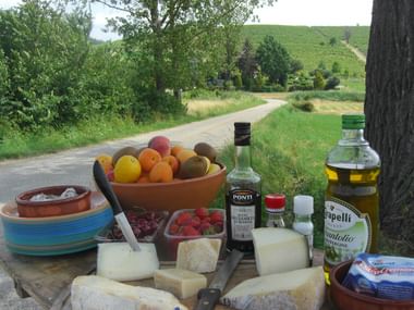 Picnic table with fresh fruits, cheese, wine bottles and local products set up along a rural road in Piedmont, Italy.