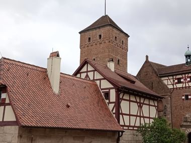 Historische Nürnberger Kaiserburg mit Fachwerkhäusern, roten Ziegeldächern und einem Steinturm unter bewölktem Himmel.