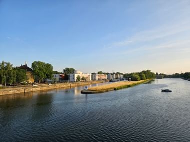 Blick auf den Main in Schweinfurt mit einer kleinen grasbewachsenen Insel, Ufergebäuden und einem Boot auf dem ruhigen Wasser unter blauem Himmel.