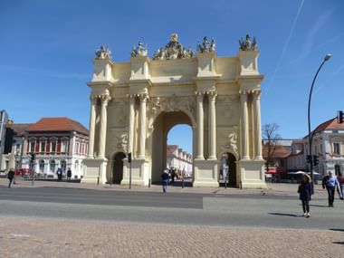 Brandenburger Tor Potsdam, ein barocker Triumphbogen mit verzierten Säulen und Skulpturengruppen oben, umgeben von historischen Gebäuden.