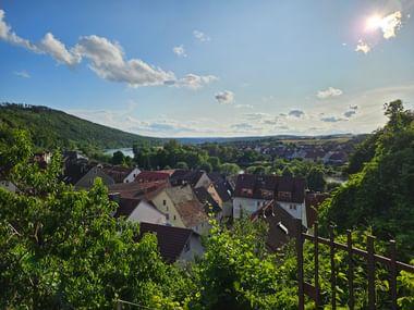 Panoramablick über die Dächer von Homburg mit dem Main und bewaldeten Hügeln im Hintergrund unter blauem Himmel mit weißen Wolken.