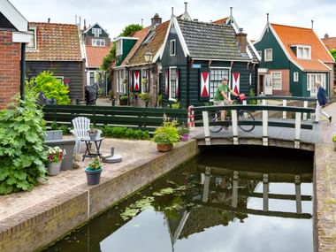 Picturesque canal scene in Volendam with traditional Dutch houses featuring colorful shutters, a wooden bridge, and visitors walking along the waterway.