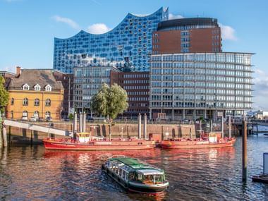 Hamburger Hafen mit Booten auf der Elbe und der markanten gläsernen Elbphilharmonie, die über historischen Backsteingebäuden aufragt.