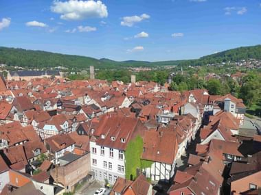 Luftaufnahme von Hannoversch Münden mit traditionellen Fachwerkhäusern mit roten Ziegeldächern, Kirchtürmen und grünen Hügeln im Hintergrund.