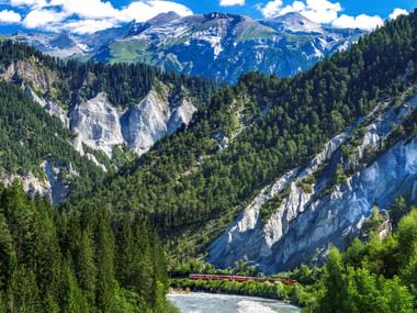 Panoramablick auf die Schweizer Rheinschlucht mit weißen Kalksteinfelsen, dichten grünen Wäldern, gewundenem Fluss und schneebedeckten Alpen.