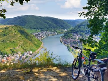 Black bicycle parked on viewpoint overlooking Moselle River valley near Cochem, with terraced vineyards on hillsides and town below.