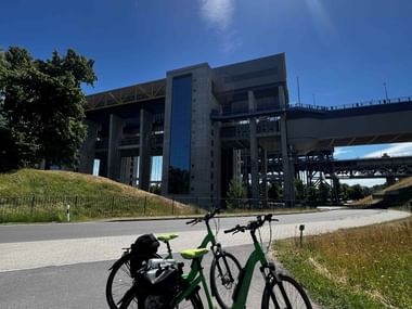 Grünes Tourenrad mit Packtaschen auf Weg vor modernem Schiffshebewerk unter strahlend blauem Himmel bei Berlin.