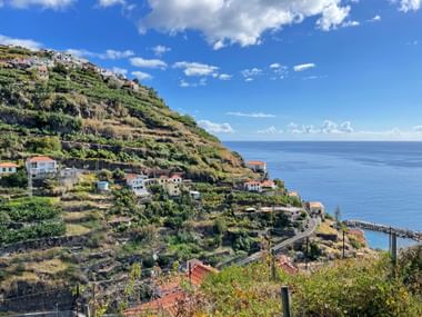 Terraced hillside in Porto Moniz, Madeira with white houses scattered among agricultural terraces overlooking the blue Atlantic Ocean.