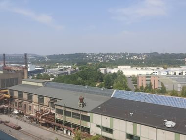 Luftaufnahme des ehemaligen Industriekomplexes Henrichshütte in Hattingen mit Fabrikgebäuden, Solarpanelen und Grünflächen unter blauem Himmel.