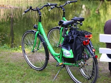 Green Velociped 7-speed touring bicycle with black panniers parked on grass near a lake, with a white bench visible in the background.