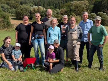 Group of adults and children posing in a meadow with forest in background. Participants of the Save the Burgwald event standing and kneeling.