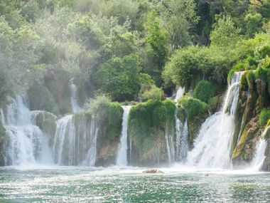Krka-Wasserfälle in Dalmatien, Kroatien Mehrere kaskadierende Wasserfälle im Krka-Nationalpark fließen über moosbewachsene Kalksteinterrassen in türkisfarbene Becken, umgeben von üppigem Wald.