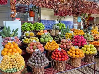 Bunte Obstauslage auf dem Funchal Monte Markt mit Weidenkörben voller Orangen, Bananen, Drachenfrucht, Avocados und tropischen Früchten.