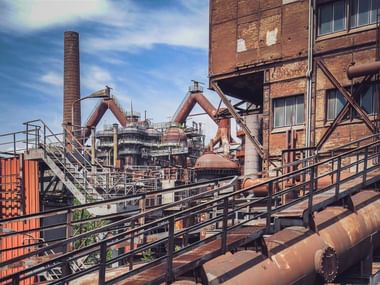 Historisches Eisenwerk Völklinger Hütte mit Backsteingebäuden, Metallstegen, Hochöfen und Industrierohren unter blauem Himmel.