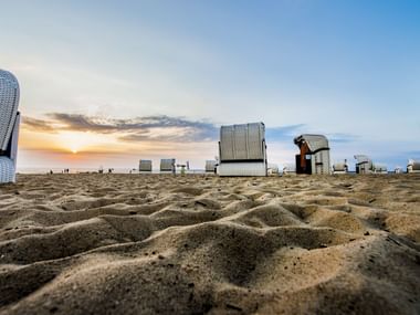 Sandstrand in Cuxhaven Sahlenburg mit traditionellen Strandkörben verteilt im Sand während des Sonnenuntergangs mit goldenem Himmel.