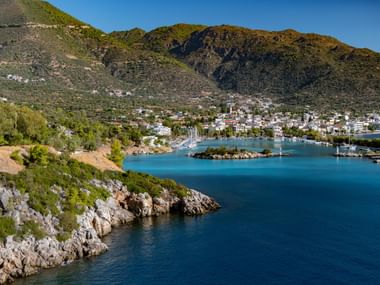 Malerische Bucht auf dem Peloponnes mit türkisfarbenem Wasser, weißen Gebäuden entlang der Küste, felsiger Küstenlinie und grünen Bergen.