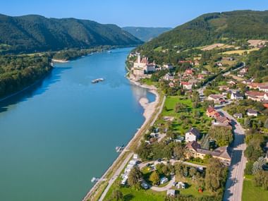 Aerial view of Schoenbuehel town in Wachau valley with castle ruins on hillside, Danube River, and forested mountains in Austria.
