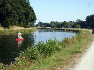 Hase-Ems-Radweg bei Osnabrück Geschotterter Radweg entlang eines Kanals mit Kanus auf dem Wasser. Dichte Bäume säumen das linke Ufer, Stromleitungen kreuzen overhead.