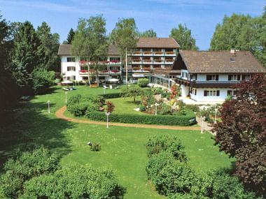 Luftaufnahme des Garden Hotel Reinhart mit traditionellen Alpengebäuden mit Balkonen, umgeben von gepflegten Rasenflächen und Gärten.