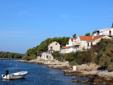 Picturesque coastal village on Solta island with stone houses along the waterfront, a white boat in the bay, and lush green vegetation.