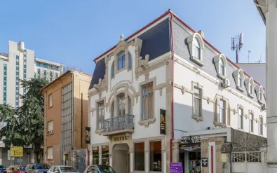 White historic building with mansard roof and ornate facade in Porto. Ground floor shows hotel entrance, upper floors feature arched windows and balcony.