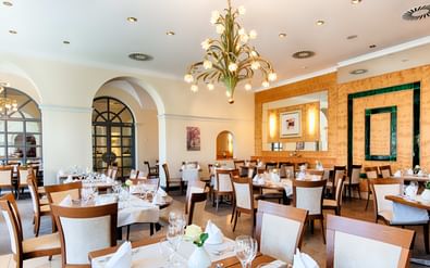 Elegantes Restaurant mit weißen Tischen, Holzstühlen, verzierten Kronleuchtern, Bogenfenstern und warmer Holzvertäfelung im Welcome Residenzschloss Bamberg.