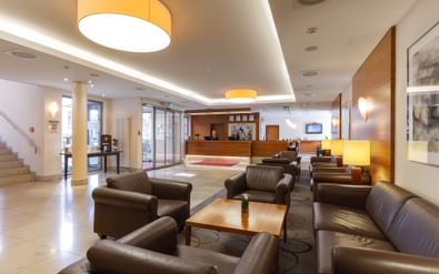 Spacious lobby of Best Western Bamberg with brown leather seating, wooden reception desk, beige tile flooring, and warm pendant lighting.