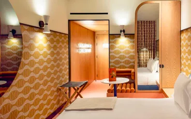 Modern hotel room at Artcore Hotel Porto with geometric patterned wallpaper, white bed, wooden wardrobe, and retro-style furnishings.