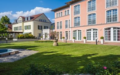 Hotel Villa Geyerswörth in Bamberg mit rosa Fassade und weißen Fenstern, angrenzendes cremefarbenes Gebäude mit grünen Fensterläden, gepflegter Rasen.