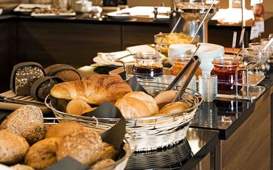 Frühstücksbuffet mit verschiedenen Brötchen und Croissants in Körben, Marmeladengläsern und Besteck im Best Western Hotel President Bonn.