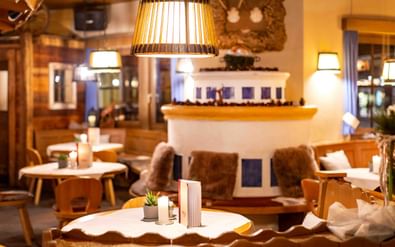 Cozy hotel lounge with wooden tables, fur-covered seating, and warm lighting. A decorative fireplace and rustic decor create an alpine atmosphere.