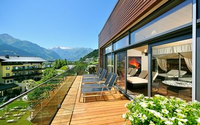 Wooden spa terrace with loungers at Hotel Schütthof in Zell am See, featuring mountain views and glass-walled relaxation rooms with curtains.