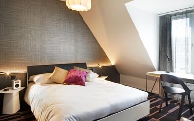 Modernes Doppelzimmer mit Dachschräge im Hotel Continental Park in Luzern mit weißer Bettwäsche, grauer Strukturtapete und Dachfenster.