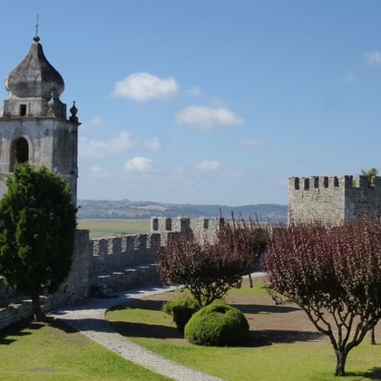 Mittelalterliches Schloss Montemor-o-Velho mit Steinturm, Zinnen und gepflegten Gärten unter blauem Himmel mit weißen Wolken.