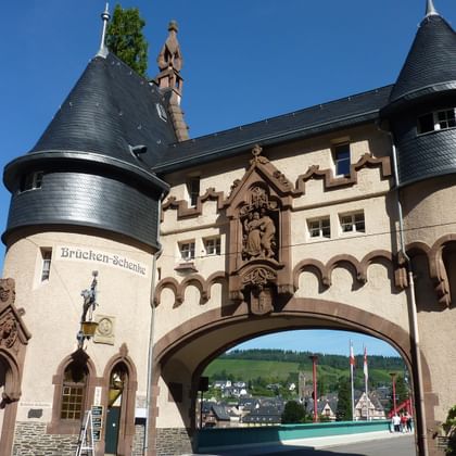 Historic Bridge Gate in Traben-Trarbach with two round towers topped by conical slate roofs, ornate stonework, and an archway spanning the street.