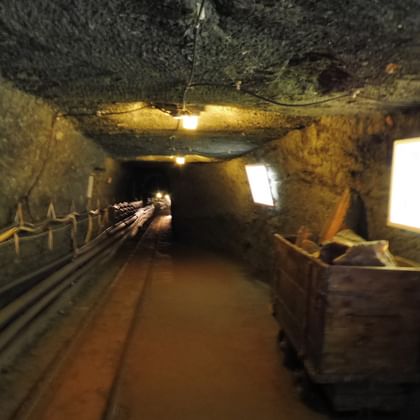 Illuminated underground tunnel in Salzbergwelten Hallein with rough rock walls, yellow handrails, and display screens along the walkway.