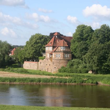Petershagen Castle by the Weser River Historic Petershagen Castle with red-tiled roofs and stone walls situated on green meadows beside the Weser River under a cloudy sky.