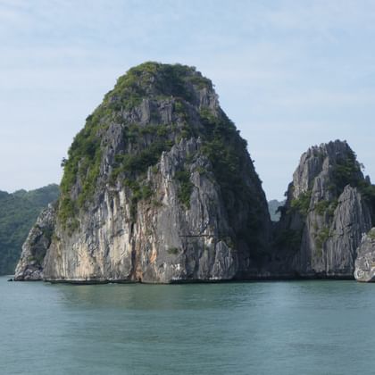 Hohe Kalkstein-Karstformationen ragen aus ruhigen türkisfarbenen Gewässern in Vietnam empor, mit üppiger grüner Vegetation auf den Felsklippen.