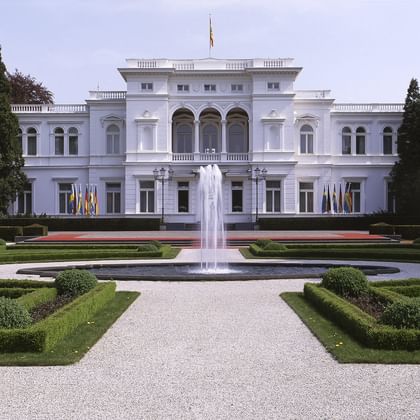 Villa Hammerschmidt in Bonn, a white neoclassical building with formal gardens, central fountain, and symmetrical landscaping with hedges.