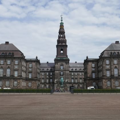Christiansborg Palace in Copenhagen with symmetrical baroque wings, central tower with green copper spire, and equestrian statue in courtyard.