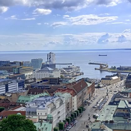 Panoramablick auf Helsingborg mit rotem Backsteinturm, historischen Gebäuden und Hafen mit Blick auf den Öresund unter bewölktem Himmel.