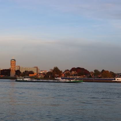 View of Dordrecht waterfront from the river showing historic brick tower, residential buildings, and cargo barges on the water under cloudy sky.