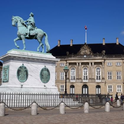 Amalienborg Palace square in Copenhagen with green patina equestrian statue on white pedestal. Yellow palace building with Danish flag visible behind.
