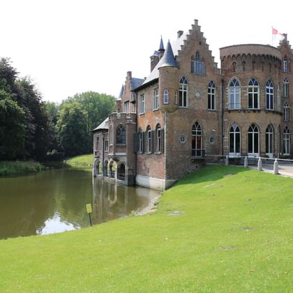 Castle Wissekerke with moat in Holland Medieval brick castle Wissekerke in Holland with Gothic windows, towers, and stepped gables, surrounded by a water moat and green lawns.