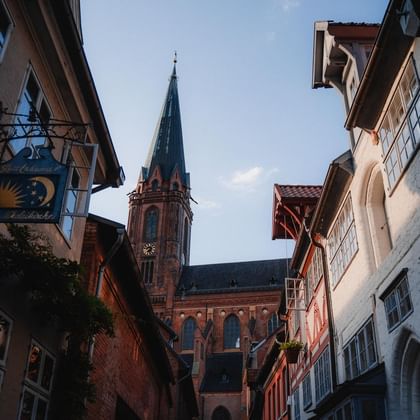 Gothic brick tower of St. Nicolai Church rising above historic half-timbered buildings in Lüneburg's old town street.